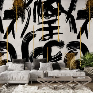 May include: A white couch with black and white throw pillows sits in front of a wall with a black and gold abstract design. The couch is in front of a coffee table with three sections.