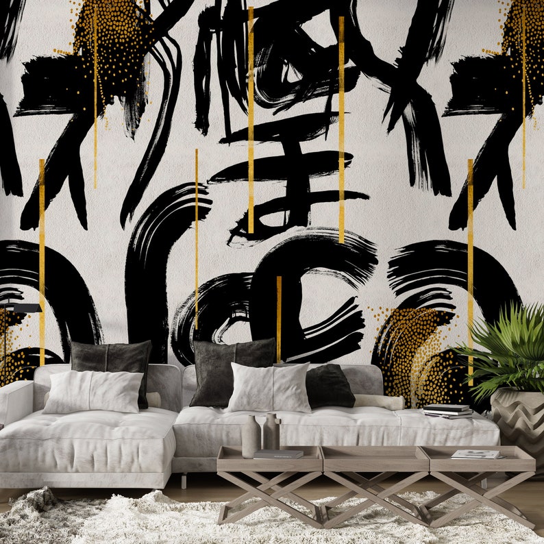 May include: A white couch with black and white throw pillows sits in front of a wall with a black and gold abstract design. The couch is in front of a coffee table with three sections.