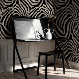 May include: A black desk with a matching stool is set against a zebra-print wallpaper. A white vase with two handles holds a dried branch. A white, textured art piece and a framed black and white image sit on the desk.