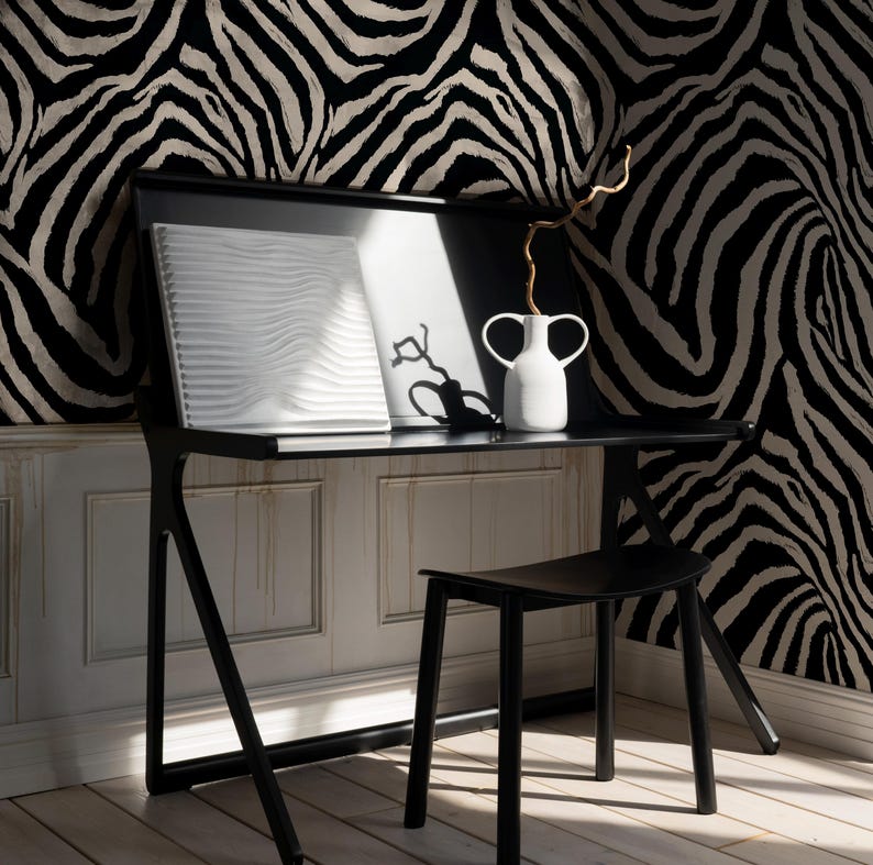 May include: A black desk with a matching stool is set against a zebra-print wallpaper. A white vase with two handles holds a dried branch. A white, textured art piece and a framed black and white image sit on the desk.