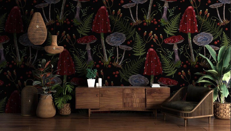 May include: A black background with a repeating pattern of red and blue mushrooms, green ferns, and red berries. A wooden cabinet with three drawers sits in front of the wallpaper. A green armchair with a woven frame sits to the right of the cabinet. Two plants in woven baskets and a lantern sit on the floor in front of the cabinet.