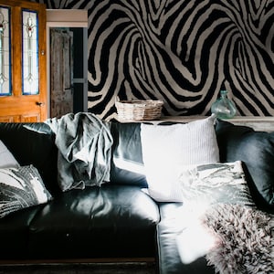May include: A black leather sectional sofa with decorative pillows and a gray throw blanket. The background features a wall with a black and white zebra stripe pattern. A woven basket and glass vase are on a shelf.