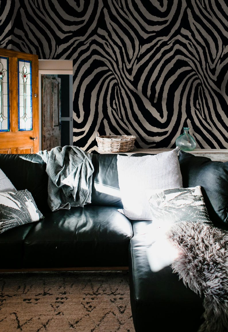 May include: A black leather sectional sofa with decorative pillows and a gray throw blanket. The background features a wall with a black and white zebra stripe pattern. A woven basket and glass vase are on a shelf.