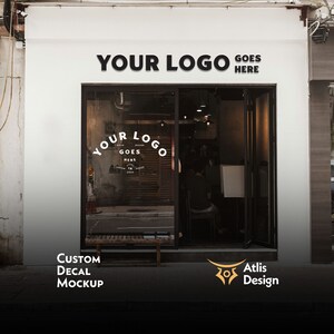 May include: A white storefront with a black sign that reads "YOUR LOGO GOES HERE". The storefront has a large glass window with a black and white decal that reads "YOUR LOGO GOES HERE". The storefront is located in a city and has a brick wall behind it. The storefront has a bench in front of it. The storefront has a sign that reads "CUSTOM DECAL MOCKUP" and a logo that reads "Atlis Design".