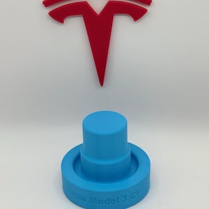 May include: A bright red Tesla logo is displayed above a light blue Tesla Model 3 GV accessory. The accessory is cylindrical with a circular base, and the text "Tesla Model 3 GV" is printed on the base.