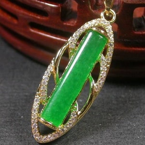 May include: A gold pendant with a green jade stone set in a delicate oval frame with clear rhinestones. The pendant is attached to a silver chain.
