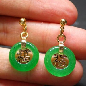 May include: A pair of green jade earrings with gold accents. The earrings are in the shape of a circle with a Chinese character for "good fortune" in the center.