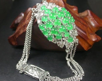 May include: A silver bracelet with a green jade pendant. The pendant is made up of many small, round jade stones set in silver. The bracelet has a chain link design.