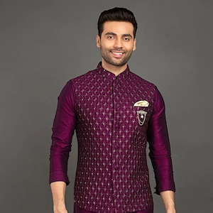 May include: A man wearing a purple kurta and matching waistcoat with gold embroidery. He is also wearing cream pants and brown shoes.