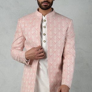 以下が含まれることがあります： 白い葉の模様が刺繍された明るいピンク色のジャケット。白いシャツとパンツの上に着用。ジャケットはマンダリンカラーで、ボタンで留めます。フォーマルでエレガントな装いです。