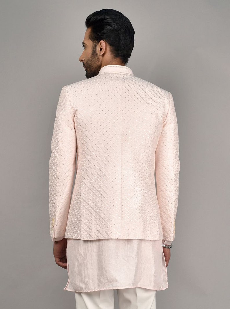Puede incluir: Una chaqueta rosa claro con un patr&oacute;n acolchado y un cuello mandar&iacute;n. La chaqueta se lleva sobre una camisa rosa claro a juego y pantalones blancos.