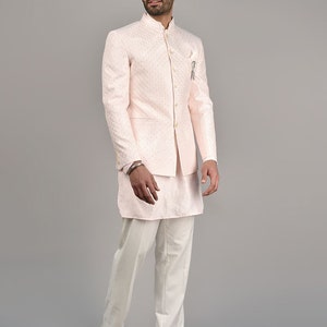Puede incluir: Una chaqueta rosa con estampado, cuello mandar&iacute;n y kurta y pantalones blancos. El atuendo es de estilo tradicional indio.