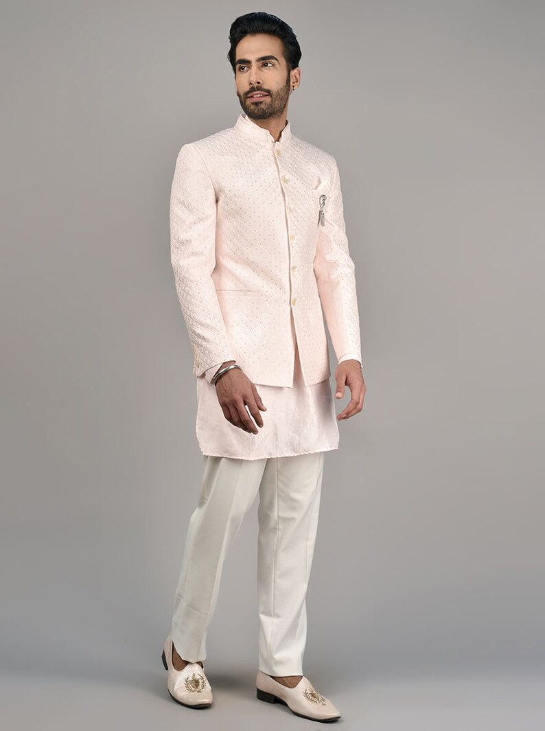 Puede incluir: Una chaqueta rosa con estampado, cuello mandar&iacute;n y kurta y pantalones blancos. El atuendo es de estilo tradicional indio.