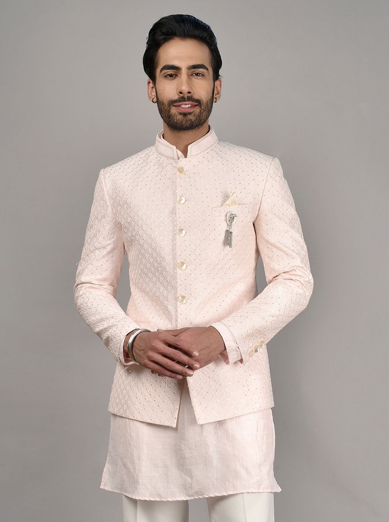 Puede incluir: Una chaqueta rosa claro con cuello mandar&iacute;n y cierre de botones. La chaqueta tiene un sutil patr&oacute;n bordado y se combina con una kurta larga rosa claro a juego.