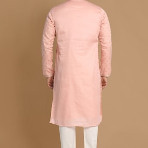 Op de afbeelding: Een roze langarmige kurta met een witte kraag en gouden borduurwerk. De kurta wordt gedragen over een witte broek.
