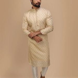 Op de afbeelding: Een cr&egrave;mekleurige, langarmige kurta met een knoopsluiting en een subtiel patroon. De kurta wordt gecombineerd met een witte broek en goudkleurige schoenen.