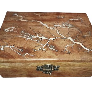 May include: Wooden box featuring a lightning pattern on the lid. The box is crafted from light brown wood with a white design. It has a metal clasp and hinges, and is suitable for storing small items.