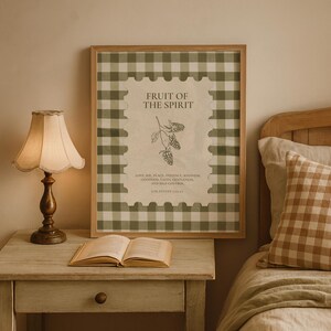 Könnte beinhalten: Ein gerahmter Druck mit dem Text "FRUIT OF THE SPIRIT" und einer botanischen Illustration. Der Rahmen hat ein grün-weißes Vichy-Muster. Ein Nachttisch mit einer Lampe und einem offenen Buch befindet sich im Vordergrund.
