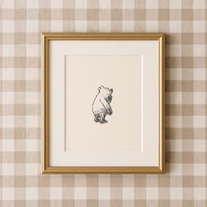 Könnte beinhalten: Gerahmte Schwarz-Weiß-Illustration eines Bären in einem goldenen Rahmen. Der Bär ist in einem einfachen, klassischen Stil gezeichnet, mit der Pfote zum Gesicht erhoben. Der Rahmen ist rechteckig und hat eine goldene Oberfläche.