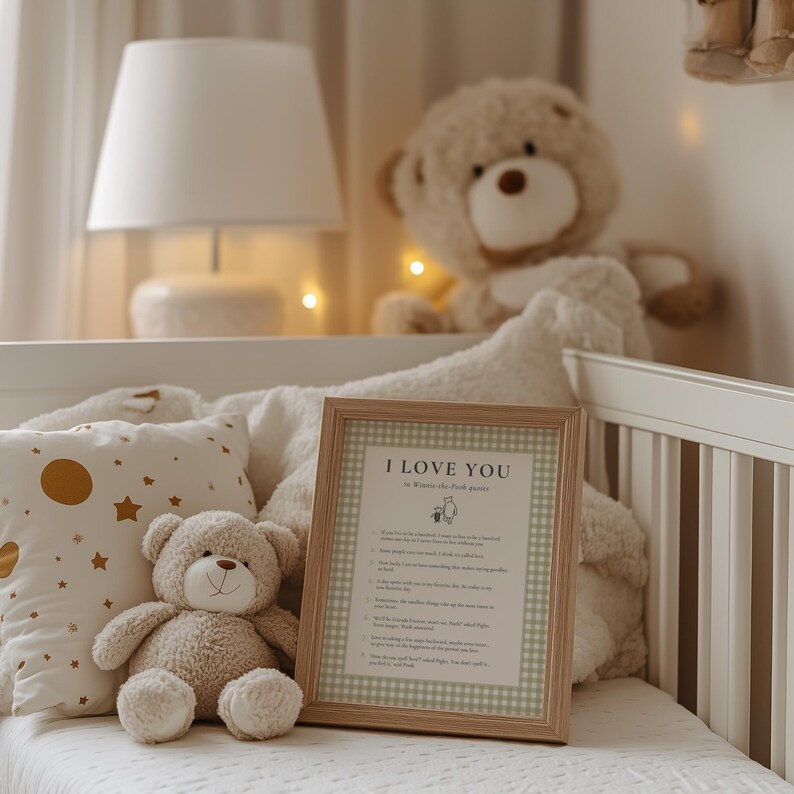 K&ouml;nnte beinhalten: Ein gerahmter Druck mit dem Text "I LOVE YOU" in einem hellen Holzrahmen, der auf einem wei&szlig;en Kinderbett liegt. Ein Teddyb&auml;r und ein Kissen mit goldenen Sternen befinden sich im Vordergrund. Ein gro&szlig;er Teddyb&auml;r sitzt im Hintergrund.