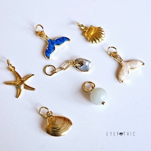 Peut inclure: Un ensemble de breloques dorées sur le thème de la mer. Les breloques comprennent une étoile de mer, une coquille, une queue de sirène et une petite perle ronde. Les breloques sont parfaites pour ajouter une touche de fantaisie aux bijoux ou autres objets artisanaux.
