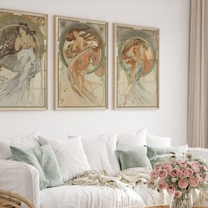 Puede incluir: Tres impresiones de arte enmarcadas que presentan ilustraciones de estilo Art Nouveau de mujeres con vestidos fluidos. Las impresiones est&aacute;n en una paleta de colores claros y vintage con acentos dorados.