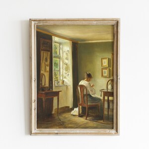 May include: A painting of a woman sitting at a table in a room with a window. The woman is wearing a white dress and is sewing. The room is decorated with a mirror and two framed pictures.