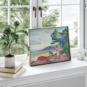 May include: A framed painting of a seascape with two figures in the foreground. The painting is done in a pointillist style with a bright color palette. The figures are wearing white clothing and are standing on a rocky shore. The sea is a vibrant blue and the sky is a soft blue with pink and purple clouds.
