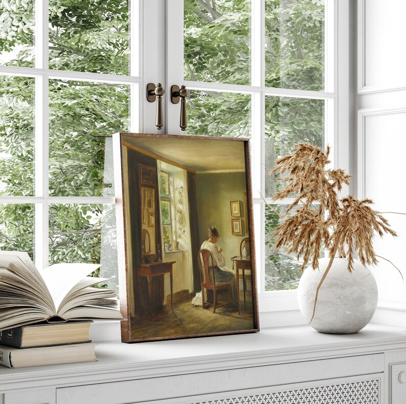May include: A framed painting of a woman sitting at a table in a room with a window. The woman is wearing a light-colored dress and is sewing. The room is decorated with a mirror and a few other pieces of furniture.