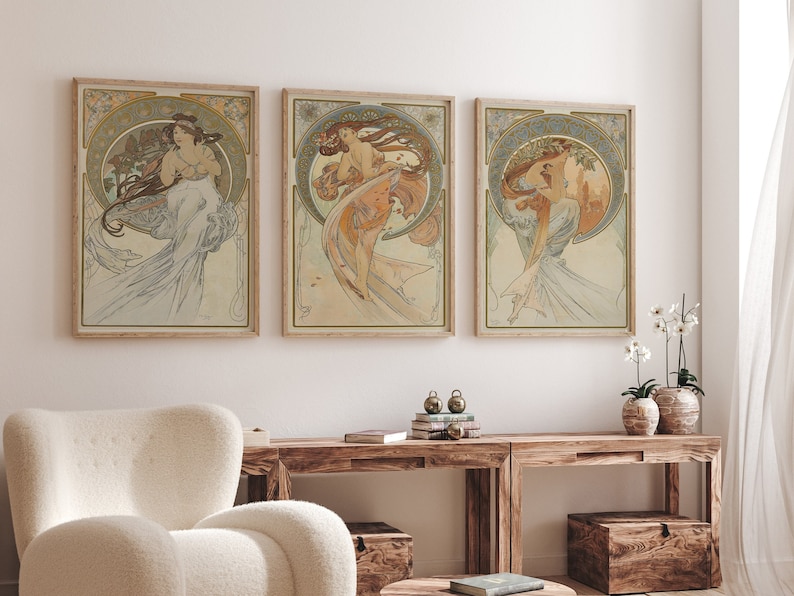 Puede incluir: Tres impresiones de arte enmarcadas que presentan ilustraciones de estilo Art Nouveau de mujeres con vestidos fluidos. Las impresiones est&aacute;n en un marco de madera claro y est&aacute;n colgadas en una pared blanca.