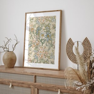 Puede incluir: Una impresi&oacute;n art&iacute;stica enmarcada con un dise&ntilde;o floral sobre un fondo crema, adornada con flores rosas, azules y verdes. La impresi&oacute;n est&aacute; en un marco de madera marr&oacute;n claro, colocada sobre un mueble de madera.