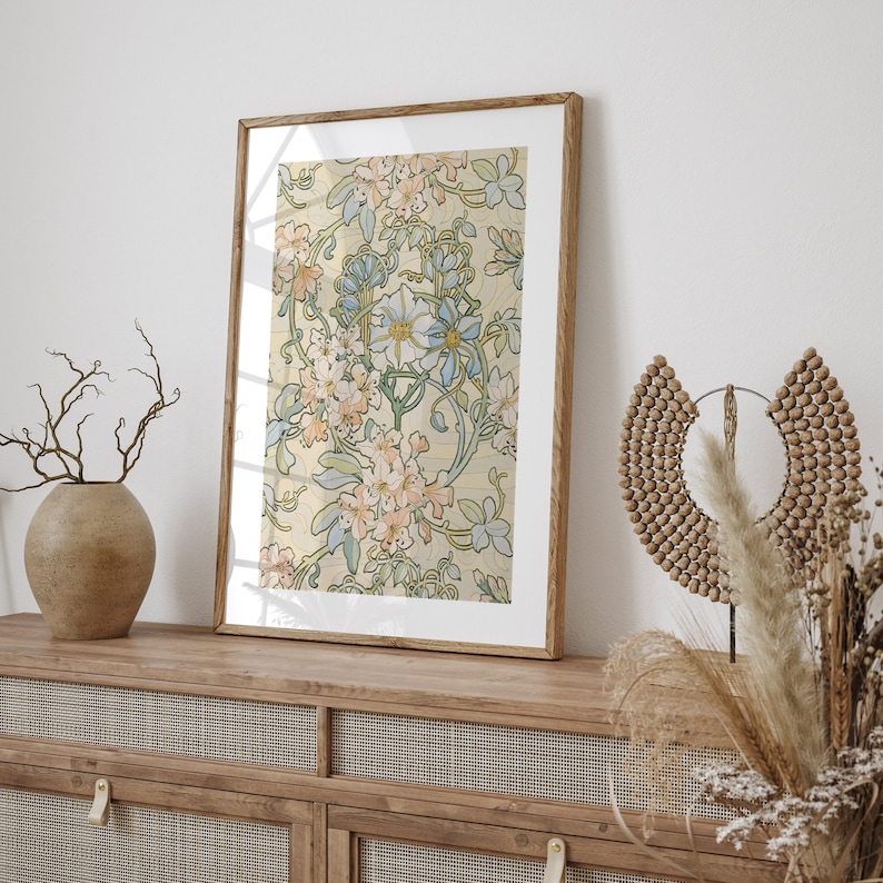 Puede incluir: Una impresi&oacute;n art&iacute;stica enmarcada con un dise&ntilde;o floral sobre un fondo crema, adornada con flores rosas, azules y verdes. La impresi&oacute;n est&aacute; en un marco de madera marr&oacute;n claro, colocada sobre un mueble de madera.