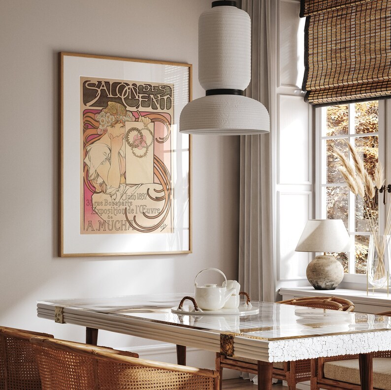May include: A white ceramic pendant light hangs over a white marble dining table with a wooden base. The table is set with a white teapot and two white cups. A framed poster with the text "Salon des Cent" and an illustration of a woman is on the wall behind the table.