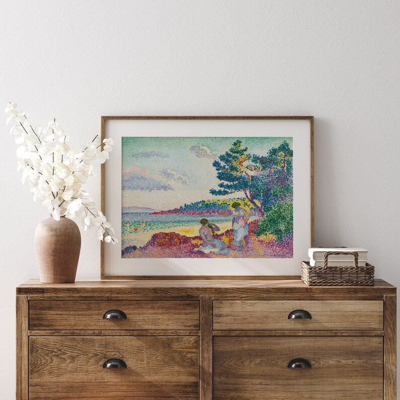 May include: A framed print of a painting depicting three figures in a landscape setting. The figures are standing and sitting near a tree on a beach. The sky is blue with white clouds. The water is a light blue color. The painting is done in a pointillist style.