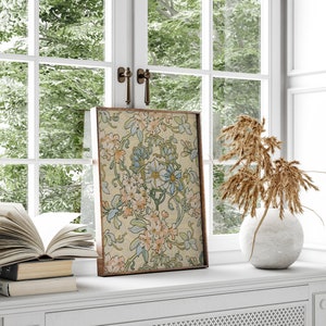 Puede incluir: Una impresi&oacute;n art&iacute;stica floral enmarcada con un fondo crema y dise&ntilde;os florales en azul claro, melocot&oacute;n y verde. La obra de arte se exhibe en un alf&eacute;izar blanco, junto a un jarr&oacute;n con plantas secas y una pila de libros.