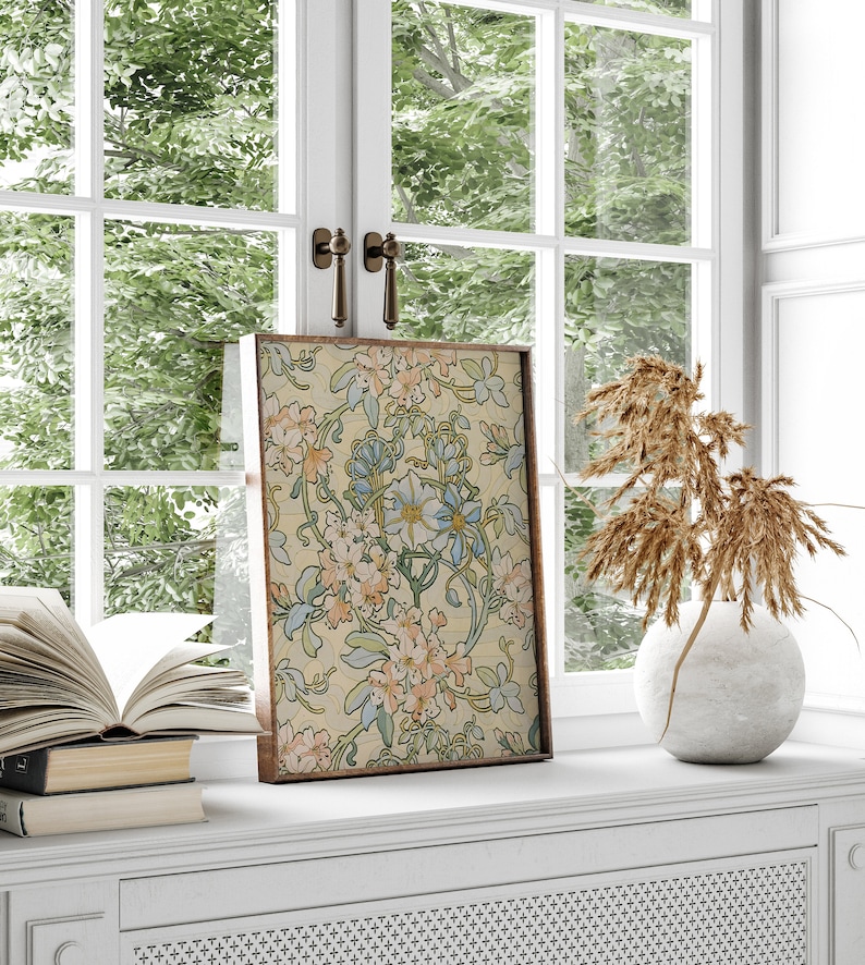Puede incluir: Una impresi&oacute;n art&iacute;stica floral enmarcada con un fondo crema y dise&ntilde;os florales en azul claro, melocot&oacute;n y verde. La obra de arte se exhibe en un alf&eacute;izar blanco, junto a un jarr&oacute;n con plantas secas y una pila de libros.