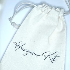 May include: A white cotton drawstring bag with the text "Hangover Kit" written in black cursive.