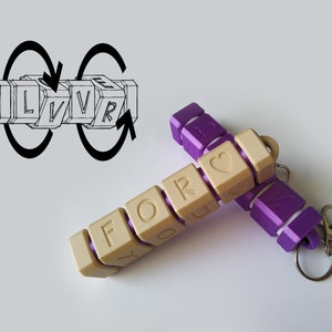 May include: Two keychains with rotating cubes that spell out "FOR YOU" and "LOVE" with a heart symbol. The keychains are made of beige and purple plastic.