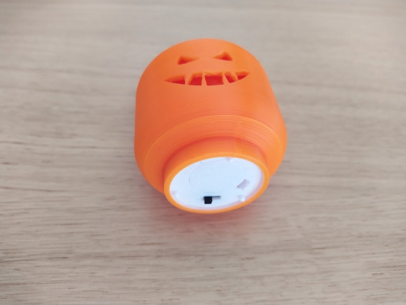 May include: An orange plastic jack-o'-lantern with a carved face and a white light-up base. The base has a small black switch.
