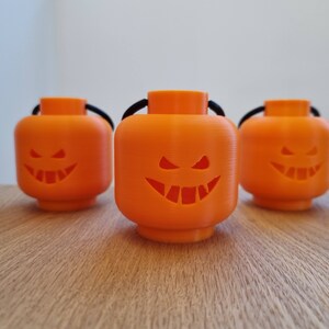 May include: Three orange Halloween jack-o'-lantern decorations shaped like Lego minifigure heads with black string handles.