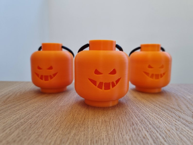 May include: Three orange Halloween jack-o'-lantern decorations shaped like Lego minifigure heads with black string handles.