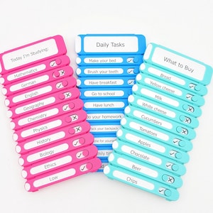 Puede incluir: Tres tableros de lista de control de plástico en rosa, azul y azul claro. El tablero rosa dice Today I'm Studying, el azul Daily Tasks y el azul claro What to Buy. Cada tablero cuenta con deslizadores para marcar las tareas completadas.