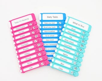May include: Three plastic checklist boards with sliding buttons. The pink board is labeled Today I'm Studying, the blue board Daily Tasks, and the teal board What to Buy. Each board features a list of items with individual sliders to mark tasks.