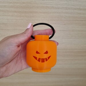 May include: Orange Halloween lantern with a black handle and a carved jack-o'-lantern face.