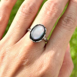 Può includere: Un anello d'argento con un'incisione ovale in madreperla di abalone iridescente.