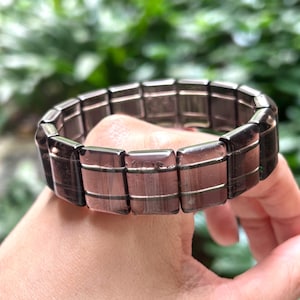 May include: A dark grey gemstone bracelet with a stretchy band. The bracelet is made of rectangular shaped stones.
