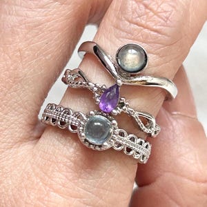 Puede incluir: Tres anillos de plata con diseños diferentes. El anillo superior tiene una piedra preciosa de amatista en forma de lágrima. El anillo del medio tiene una piedra preciosa de aguamarina redonda de color azul claro. El anillo inferior tiene una piedra preciosa de piedra lunar redonda de color gris.