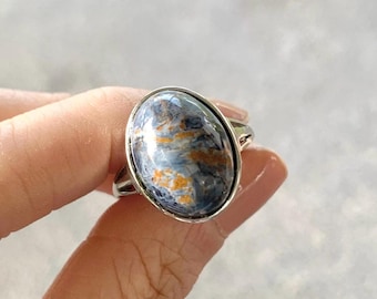 May include: Oval-shaped ring featuring a polished gemstone with blue, gray, and orange hues. The stone is set in a silver-colored metal band. The ring is a piece of jewelry.
