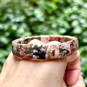 Può includere: Un braccialetto fatto di pietre quadrate multicolori. Le pietre sono un mix di rosa, rosso, bianco e nero. Il braccialetto è al polso di una persona.