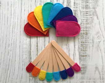 May include: A set of rainbow-colored felt hearts and wooden sticks with felt tips. The hearts are arranged in a fan shape, while the sticks are arranged in a radial pattern.